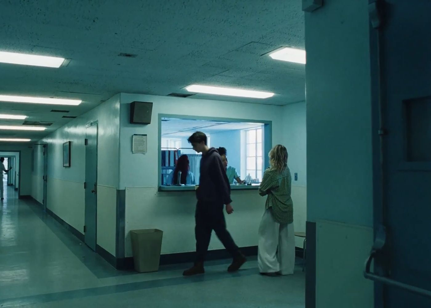 People passing a nurses' station in a blue-green hospital corridor